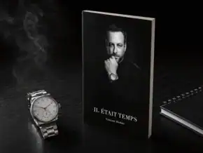 Un livre de magie noir avec portrait d'homme, montre et carnet sur une table noire.