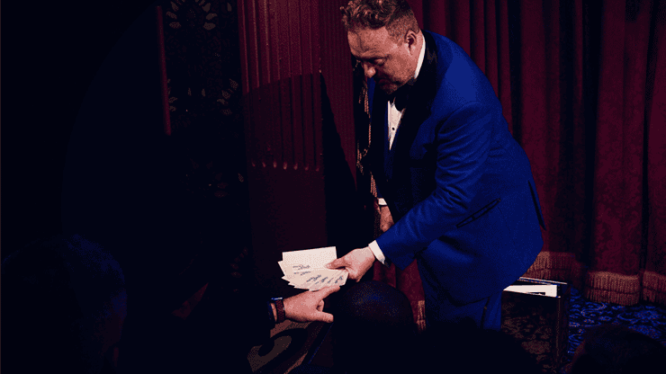 Magicien en costume bleu effectuant un tour de magie avec une carte.