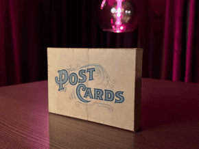 Boîte de cartes postales avec texte 'Post Cards' sur une table en bois.