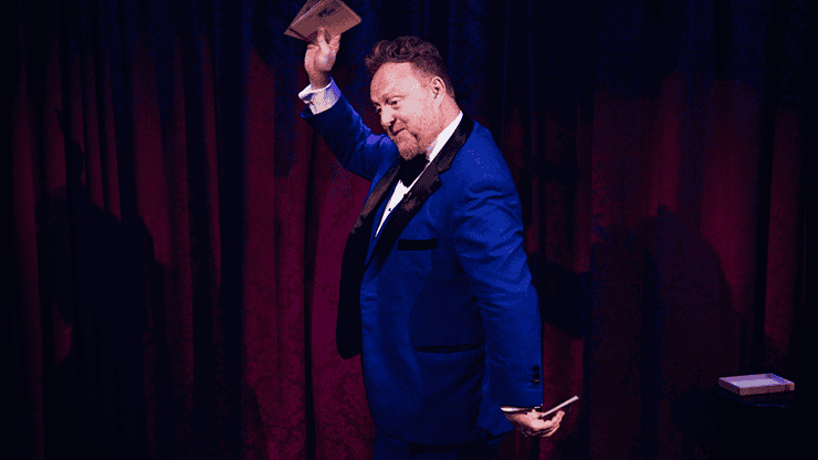 Magicien en costume bleu effectuant un tour de magie avec des cartes.